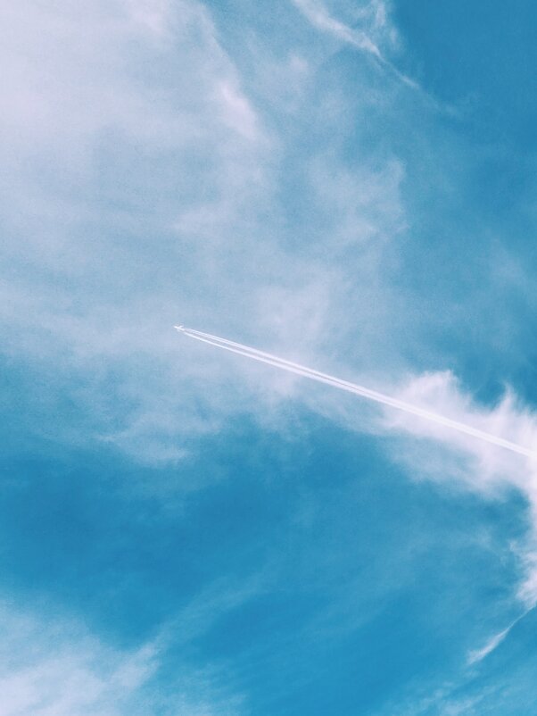 A plane flying high and far in the blue sky, leaving behind itself white lines - Roman Griev