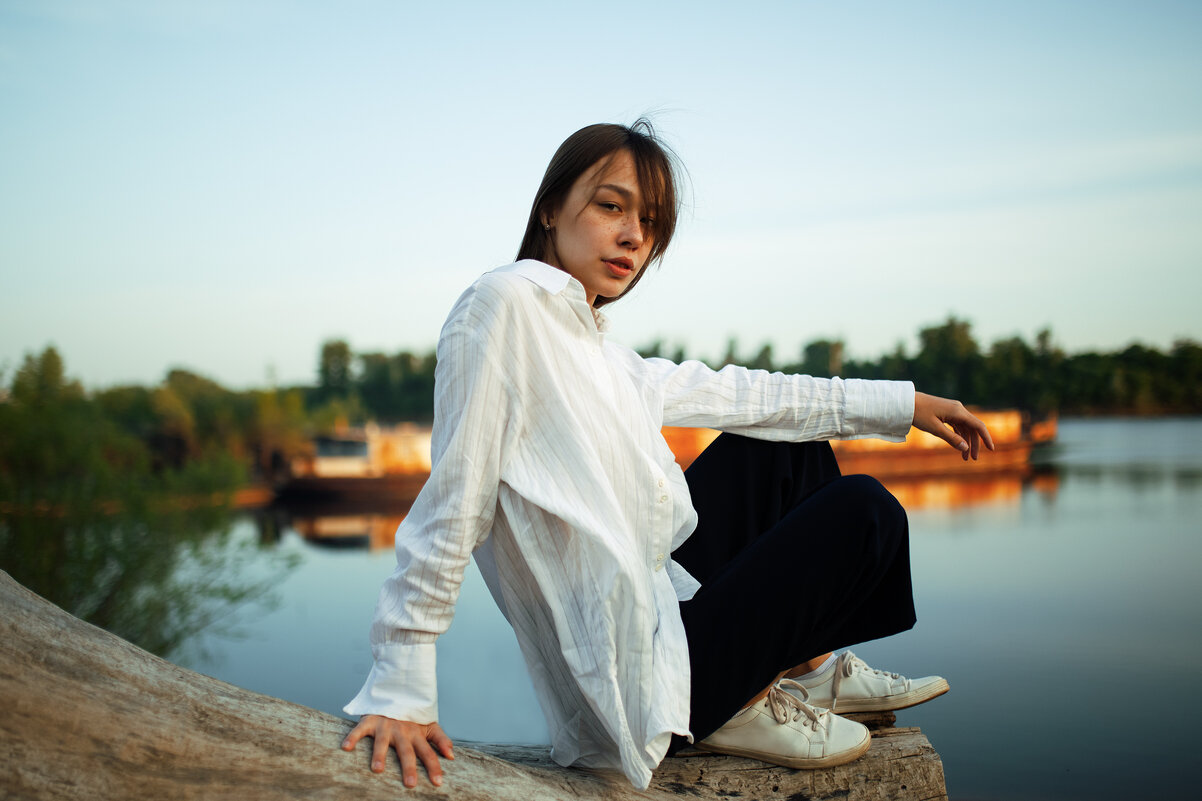 Девушка в белой рубашке сидит на бревне во время заката на фоне корабля у реки - Lenar Abdrakhmanov