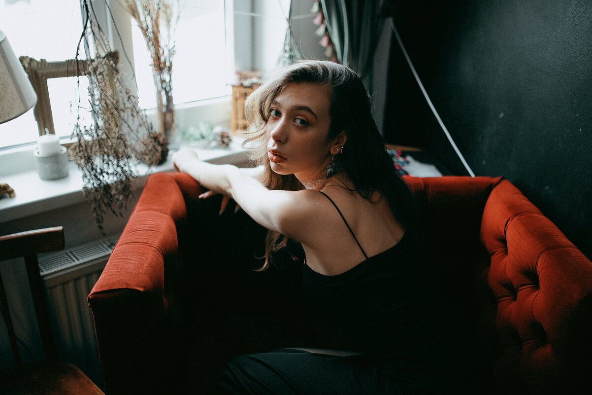 Девушка в классическом черном платье строго смотрит в камеру, сидя на красном бархатном диване - Lenar Abdrakhmanov