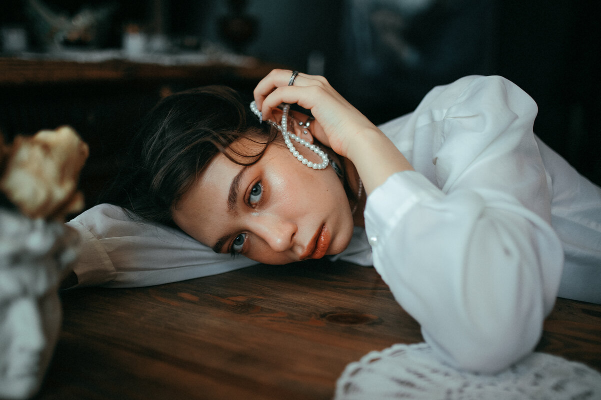 Портрет девушки, лежащей на деревянном столе, с белыми жемчужными бусами в руках - Lenar Abdrakhmanov