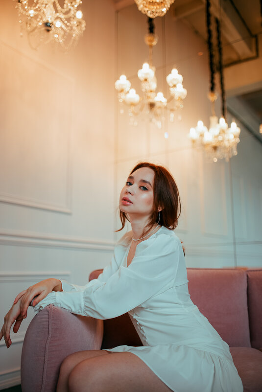 Девушка в белом платье сидит на диване в студии с роскошным интерьером - Lenar Abdrakhmanov