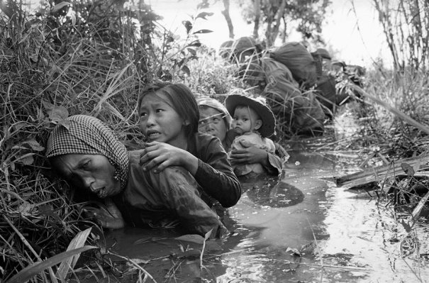 Фотографиия Хорнста Фааса,  на которой женщина и дети прячутся в канаве во время битв близ Сайгона в 1966 г